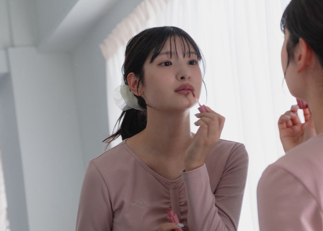 Tokimeki by mueのリップモチーフロゴ入りフィットネスウェアのピンクを着た、可愛い女の子が鏡に向かってリップを塗り直してる様子